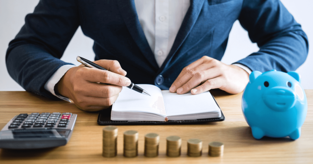 Como ser Investidor Iniciante? Homem anotando seus invetimento em umcaderno e um cofre em forma de porquinho azul