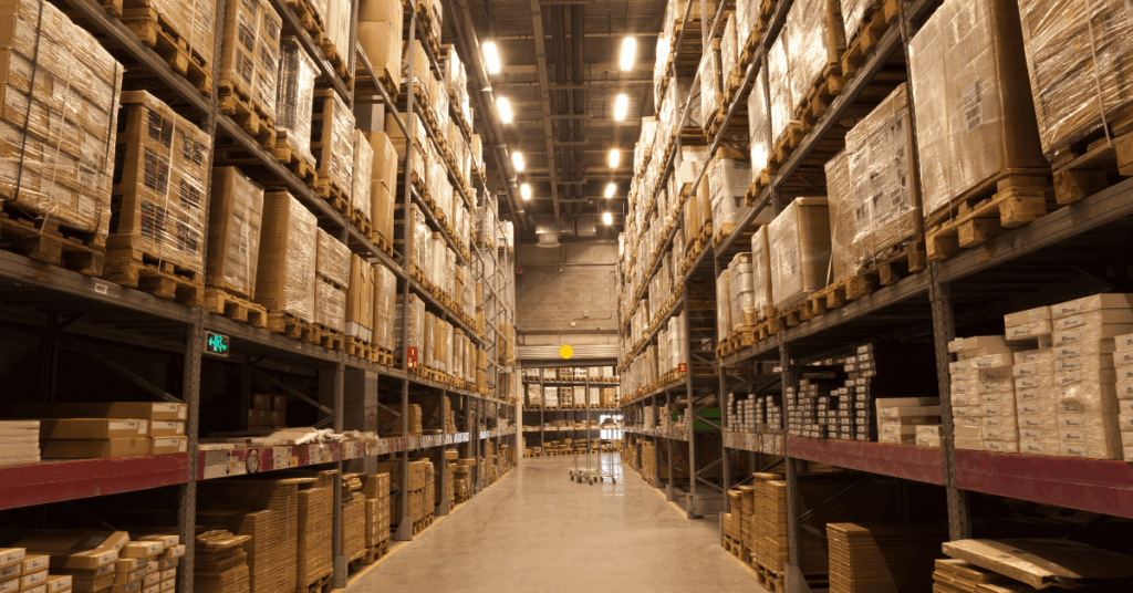 Interior de um centro logístico com prateleiras altas repletas de pallets e mercadorias armazenadas, representando os imóveis do fundo imobiliário BTLG11.